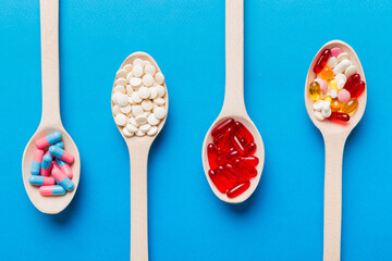 Vitamin capsules in a spoon on a colored background. Pills served as a healthy meal. Red soft gel...