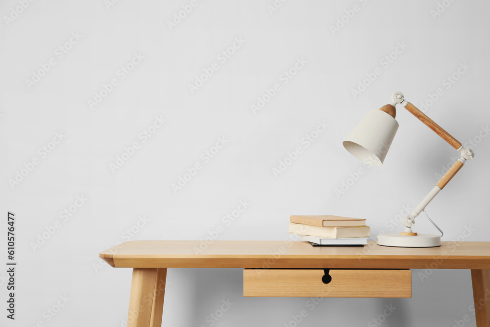 Wall mural Stylish modern desk lamp and books on wooden table near white wall