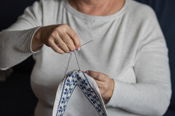 Senior woman's hands embroidering a cross-stitch floral pattern on linen fabric with needle and...