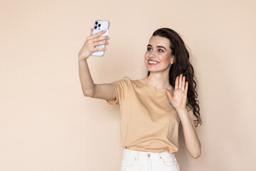 Young woman on a beige background waving her hand at the phone talking via video call