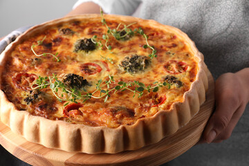 Woman holding delicious homemade vegetable quiche on light gray background, closeup