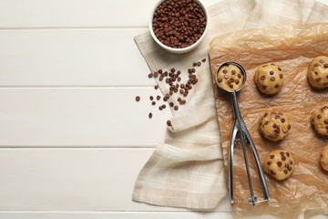 Uncooked chocolate chip cookies and scoop on white wooden table, flat lay. Space for text