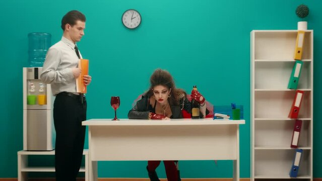 A drunk woman sits with her head on the table near a bottle of alcohol. An office worker looks at the woman indignantly. The woman rises, drinks from her throat and leaves. Advertising.