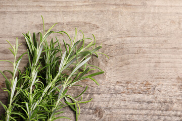 Fresh rosemary sprigs on wooden table, flat lay. Space for text