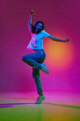 Portrait of emotive, young girl wearing casual clothes dancing over pink color studio background in...