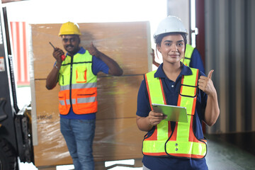 Warehouse workers woman with hard hats and reflective jackets using tablet, walkie talkie radio and...