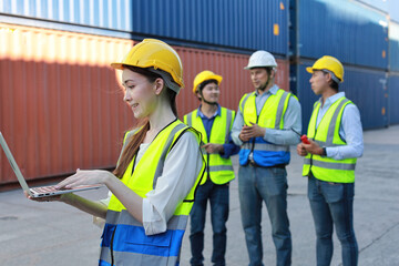 Group of multiethnic technician engineer in protective uniform standing and using computer, walkie talkie radio and tablet while.working together and controlling at container cargo site industrial