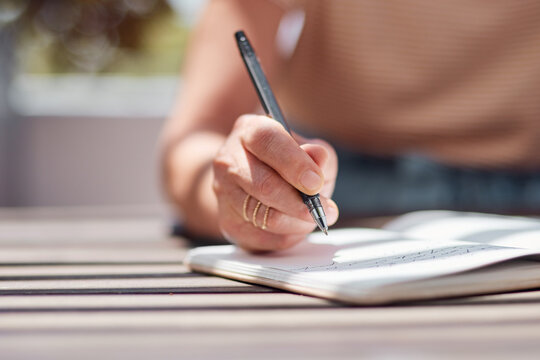 Hand, journal and book with a woman writer sitting outdoor in summer for inspiration as an author. Idea, planning and notebook with a female person using a pen to write in a planner or diary outside