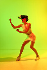 Fototapeta na wymiar Girl wearing VR headset glasses playing virtual reality game over acid green and yellow background. Youth, virtual lifestyle of future. Concept of games, unreal world