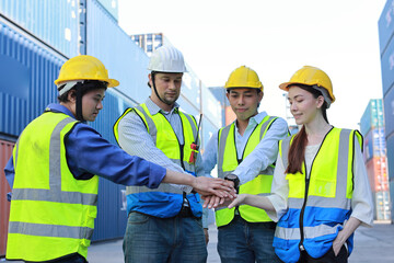Fototapeta Group of multiethnic technician engineer and businessman in protective uniform with hardhat stand and stacking hands celebrate successful together or completed deal commitment at container cargo site obraz