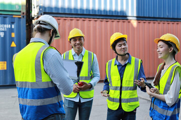 Fototapeta Group of multiethnic technician engineer in protective uniform standing and using computer, walkie talkie radio and tablet while.working together and controlling at container cargo site industrial obraz