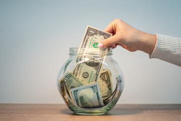 Fototapeta Close up shot of hand of a girl dropping money into a glass jar, close up, copy space. Savings, money and cash, finances, investing, growth management, income, business concept obraz