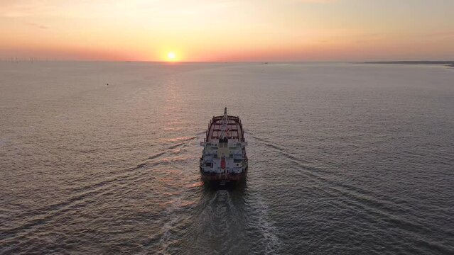Aerial view of a cargo vessel in the sea in sunset time leaving and entering container port