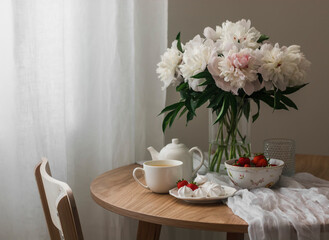 Tea party table - green tea, strawberries, meringue on a wooden table, a wooden chair, a bouquet of peonies. Cozy interior