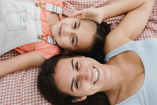 Happy teenage girl and little sister smiling on camera while lying on a towel during pic nic at city park - Family concept - Focus on child face