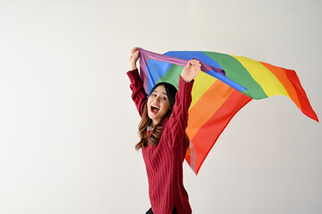 A cheerful Asian woman with a rainbow LGBT flag stands over an isolated white studio background