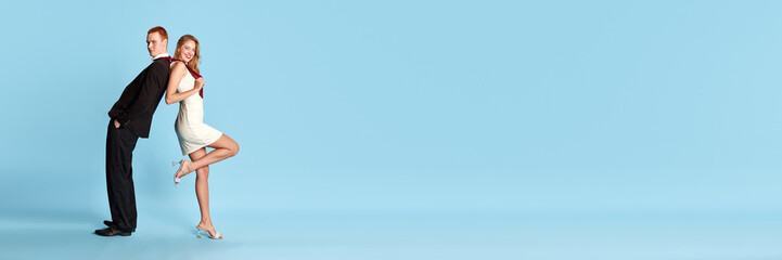 Marriage. Beautiful young couple, man and woman in stylish clothes standing back to back against blue studio background. Concept of family, relationship, youth, emotions, fun. Banner. Copy space for