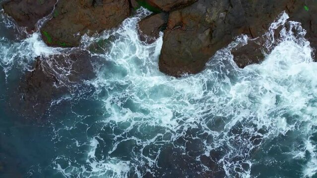 blue foamy waves crashing against a cliff - aerial video.