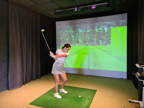 Girl playing golf on screen and golf simulator