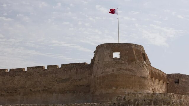 A view of Arad Fort in Bahrain. The flag of Bahrain flies above one of the towers against a blue sky.