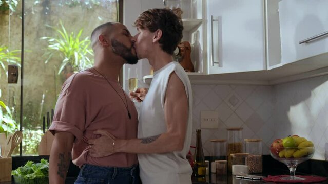 casal gay inter racial brasileiro na cozinha brindando com champanhe e se beijando no dia dos namorados