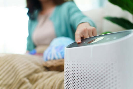 Happy Asian Young Woman Turning On High Efficiency Air Purifier While Staying And Relaxing In The Living Room. Woman Using Air Purifier In Her House.