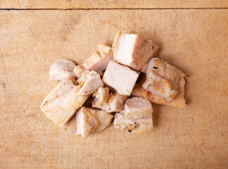 Top view of several pieces of roasted chicken breast on wood cutting board. - 610591876