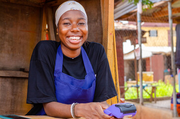 an african lady using a point of sale machine for a transaction in her kiosk