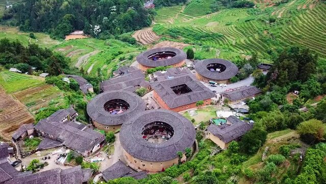 Slow orbiting aerial shot of the famous Unesco World Heritage Tulou Hakka houses. Located on a mountain hill with green terraces and fields, Fujian, China