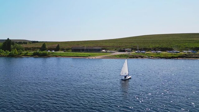 Winscar Reservoir in Yorkshire, where a boat race unfolds on the marvelous blue lake. Small one-man boats with white sails compete fiercely, making this weekend sporting event