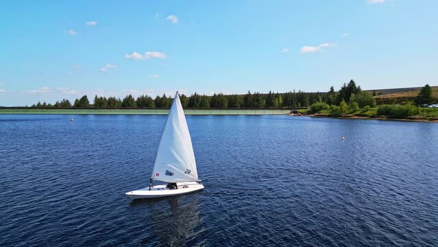 exhilarating boat race. Sailing boats, their white sails gleaming, dash across the tranquil blue lake under the bright midday sun, creating an unforgettable weekend sporting event for a sailing club.
