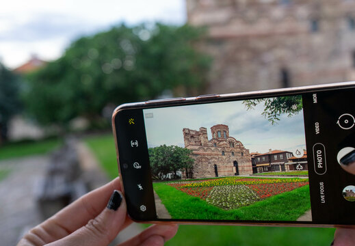 Taking photo of Church of Christ Pantocrator with smartphone in Nesebar, Bulgaria, woman hands holding mobile phone capturing ancient byzantine architecture in old town