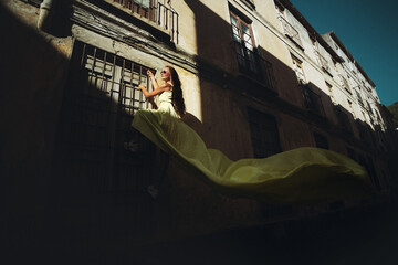 A woman in a long yellow dress is climbing a lattice window of house.