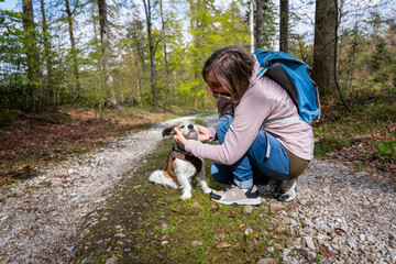 Naklejka na ściany i meble Eine Frau mit Rucksack mit einem kleinen Hund auf einem Waldweg. Pause machen, Natur.