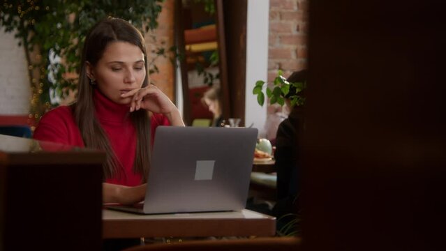 Beautiful woman is working at laptop in cafe. Stock footage. Stylish young woman is working at laptop in cafe. Beautiful woman is typing novel or working on laptop. Freelance