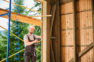 Carpenter constructing wooden framed house. Bearded man worker cladding facade of house, fastening...