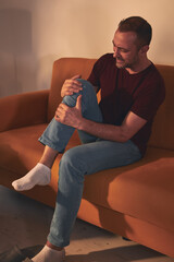 Man with knee pain sitting on a sofa at home.