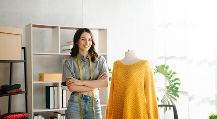 Fashion designer woman talking smart phone and using laptop with digital tablet computer in modern studio the clothes hanging on the racks .