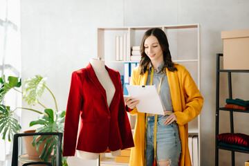 Fashion designer woman talking smart phone and using laptop with digital tablet computer in modern studio the clothes hanging on the racks .