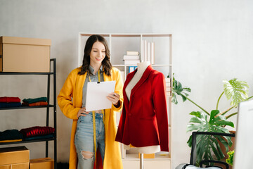 Caucasian young woman on desk in home office of fashion designer and holds tablet, laptop and...