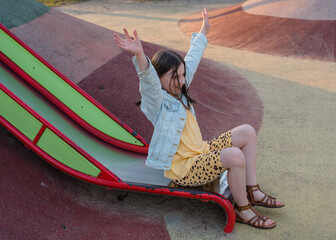 A happy girl at a playground during sunset. The girl is sliding down a slide.