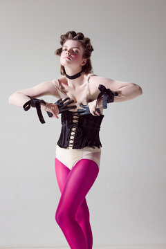 High fashion. Portrait of young extravagant girl in black corset and pink tights against grey studio background