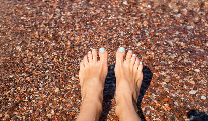 Women's feet on a pebble beach on the sea. Rest, relaxation, sunbathing. Close-up. Copy space. Selective focus.