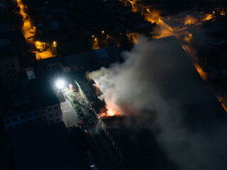 Aerial view of an industrial building that is on fire. Night fire. Smoke in the sky Strong fire in the warehouse.