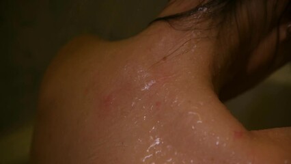 Close up of a person's neck and back under the jets of water in the shower. Close-up of a woman's body in the bathroom. A feminine back under streams of water. High quality 4k footage 