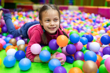 Fototapeta na wymiar Little smiling girl having fun with balls in amusement center for kids