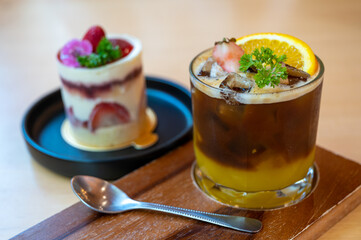 A glass of iced americano black coffee and layer of orange with sliced orange fruit