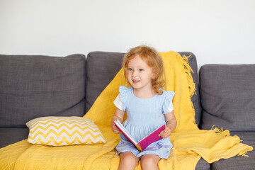 3-year-old girl sits at home on the couch with a pink glittery notebook