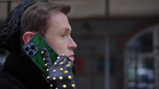 Side view closeup young LGBT man walking on urban city street talking on smartphone. Close-up portrait of Caucasian gay person with serious facial expression strolling chatting outdoors