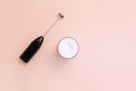 Milk foam maker with glass of milk on pink peach background.